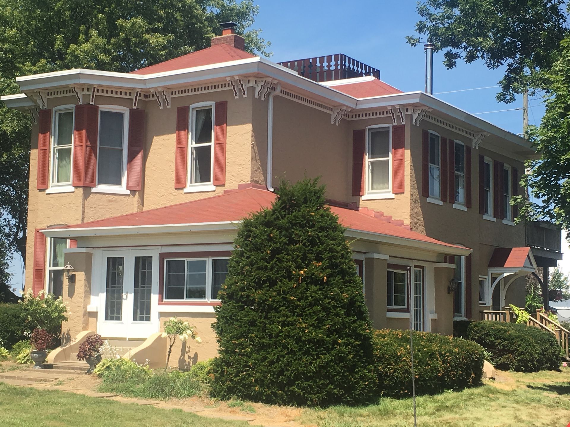 Two-story cream and red house with a red roof, white trim, and a large green bush in front