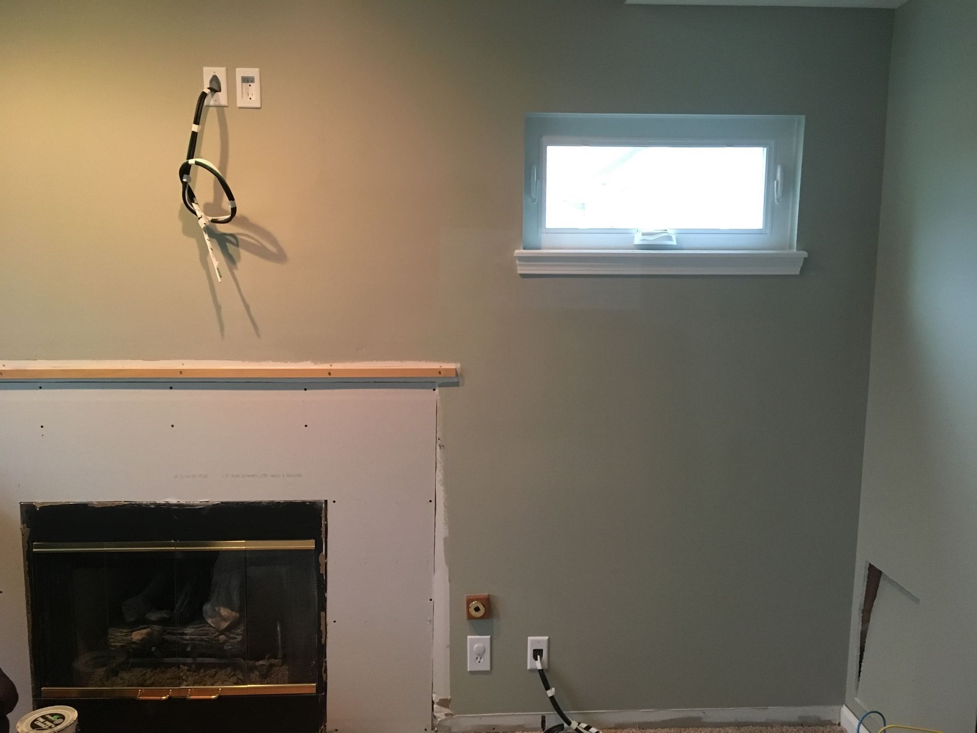 Partially renovated room with a fireplace, exposed wiring, and a small window on a gray wall.