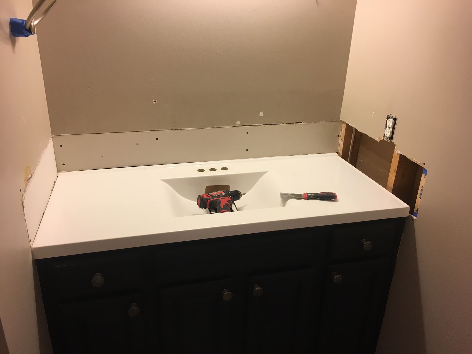 Bathroom vanity with sink cutout, tools on the counter, and unfinished wall behind it