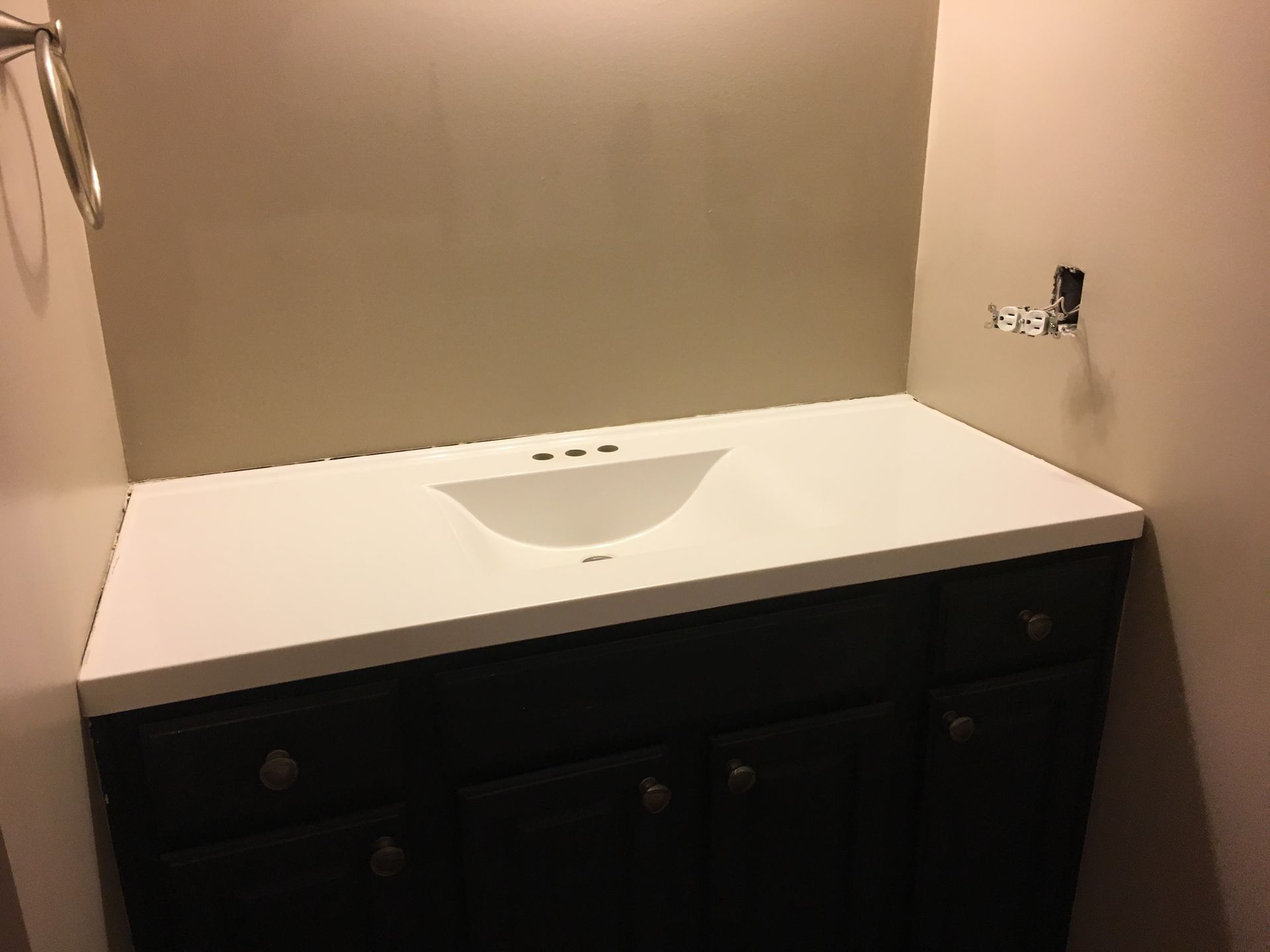 Bathroom vanity with white sink countertop, dark cabinet, and beige walls under construction