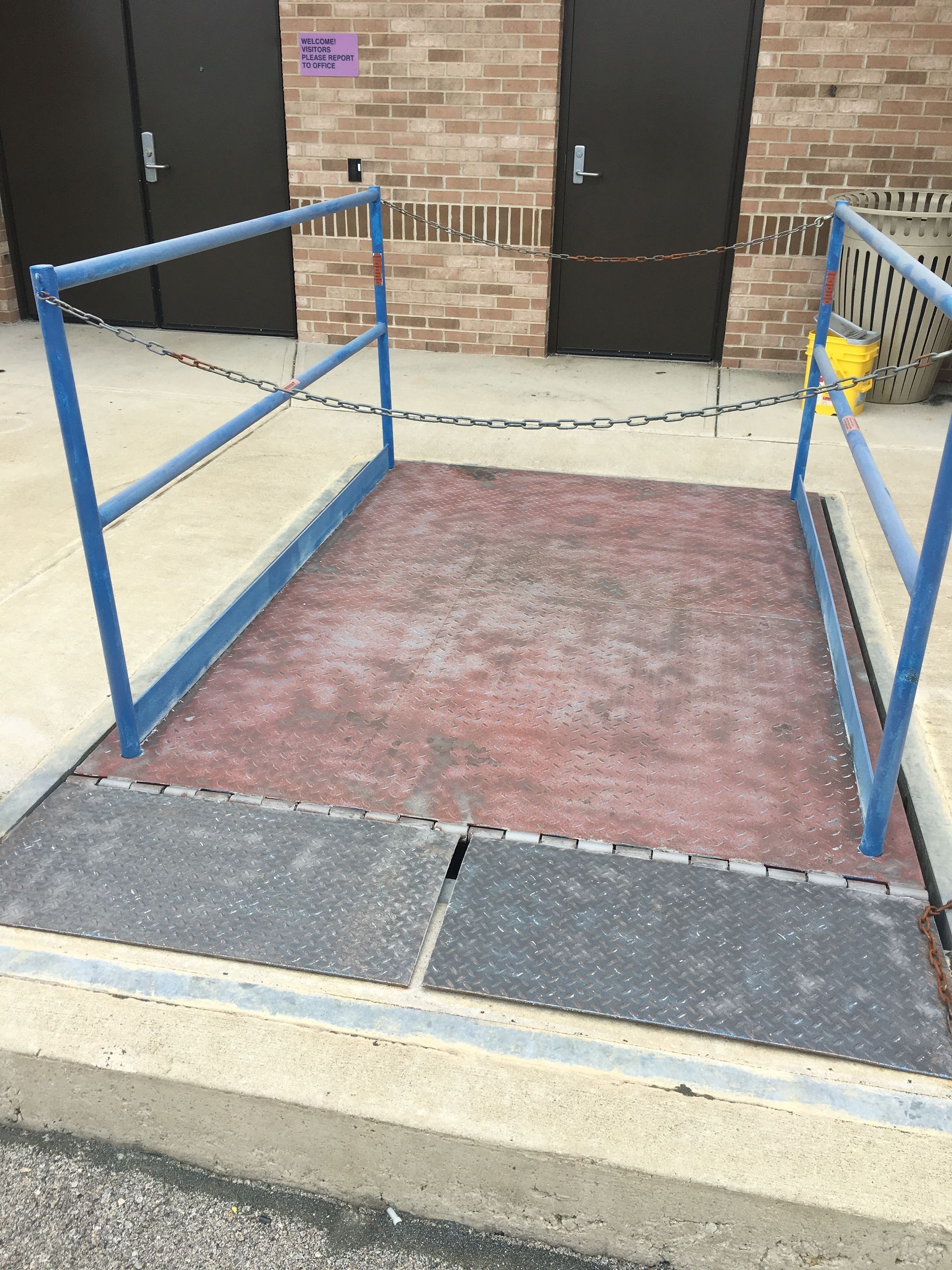 Blue handrails leading to a brick building entrance with steps and a wheelchair ramp.