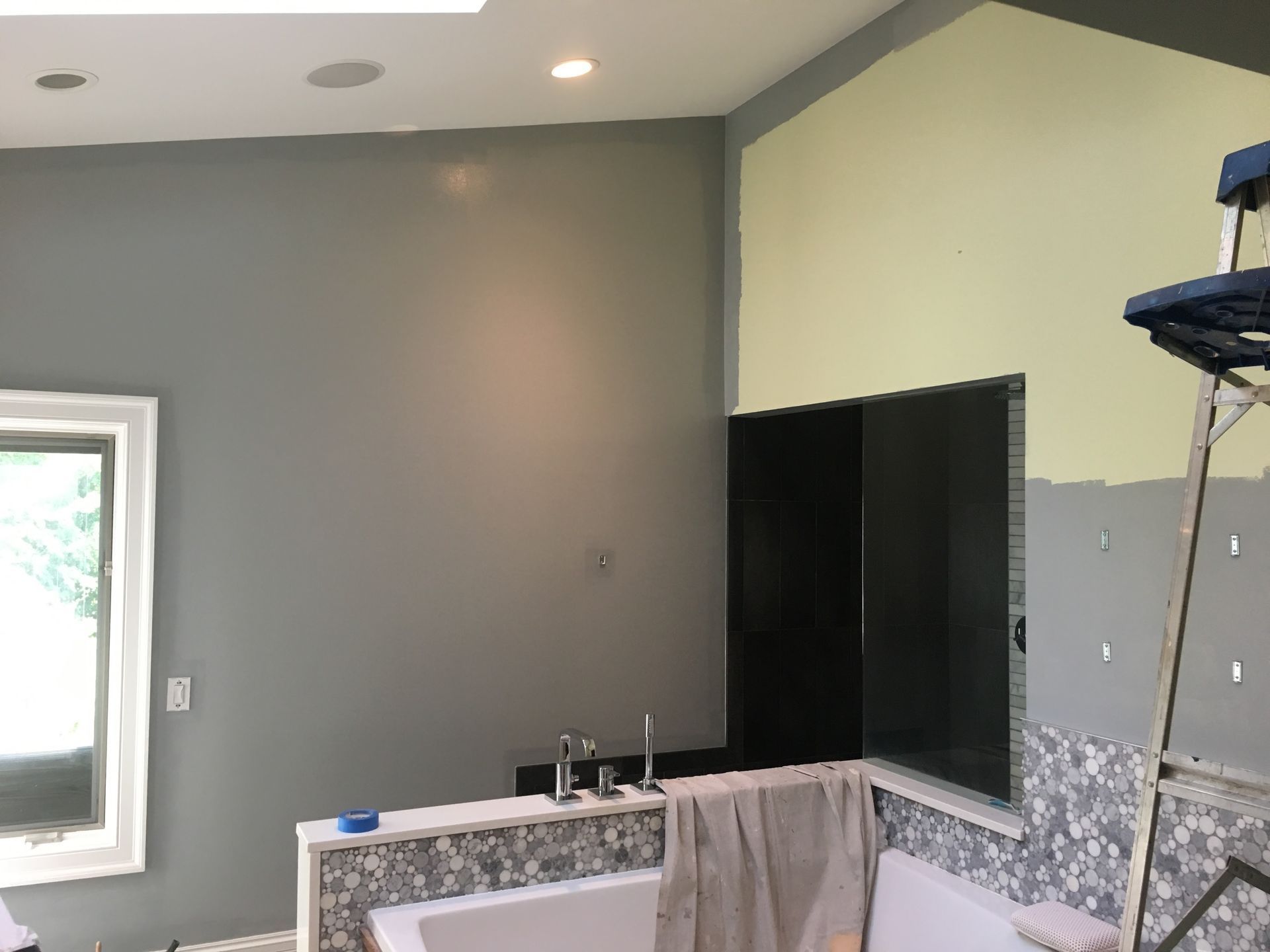 Unfinished bathroom with gray walls, tiled tub surround, and a window letting in daylight.