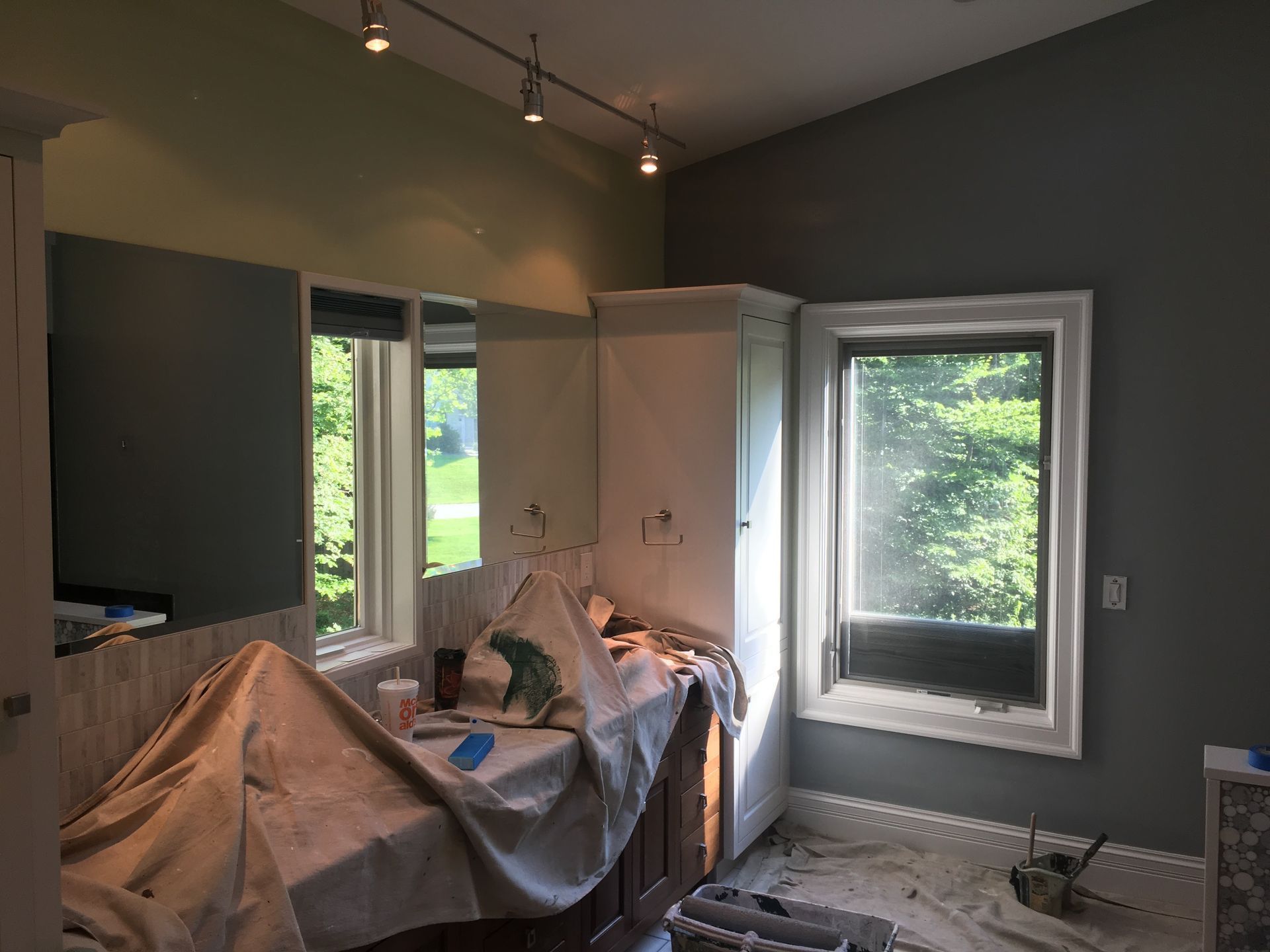 Interior room under renovation with covered furniture, gray walls, windows, and a dark accent wall