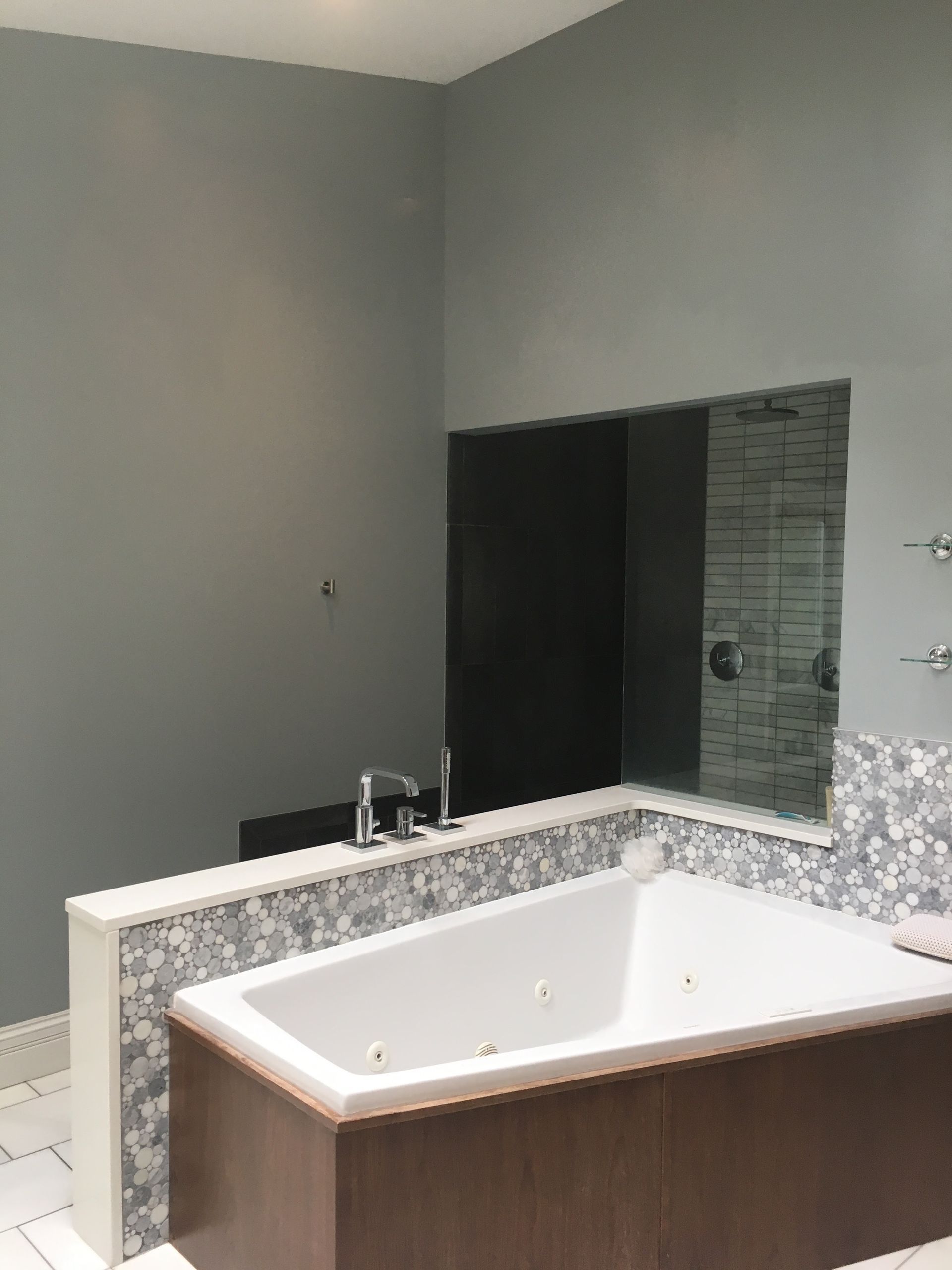 Modern bathroom with a large built-in soaking tub, gray walls, and a mosaic-tile backsplash around the mirror.