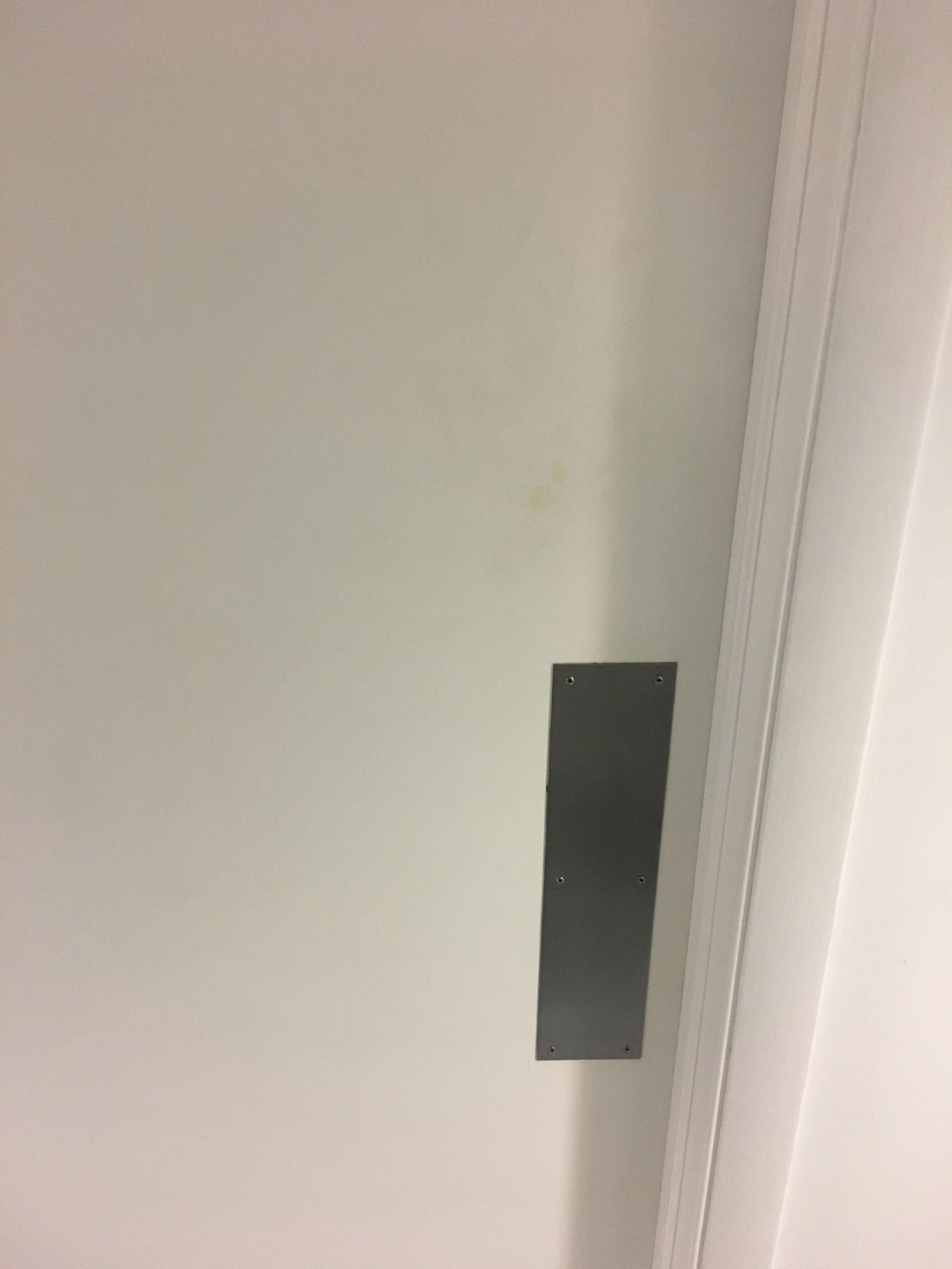 White wall with a narrow dark rectangular plate or panel near a doorway trim