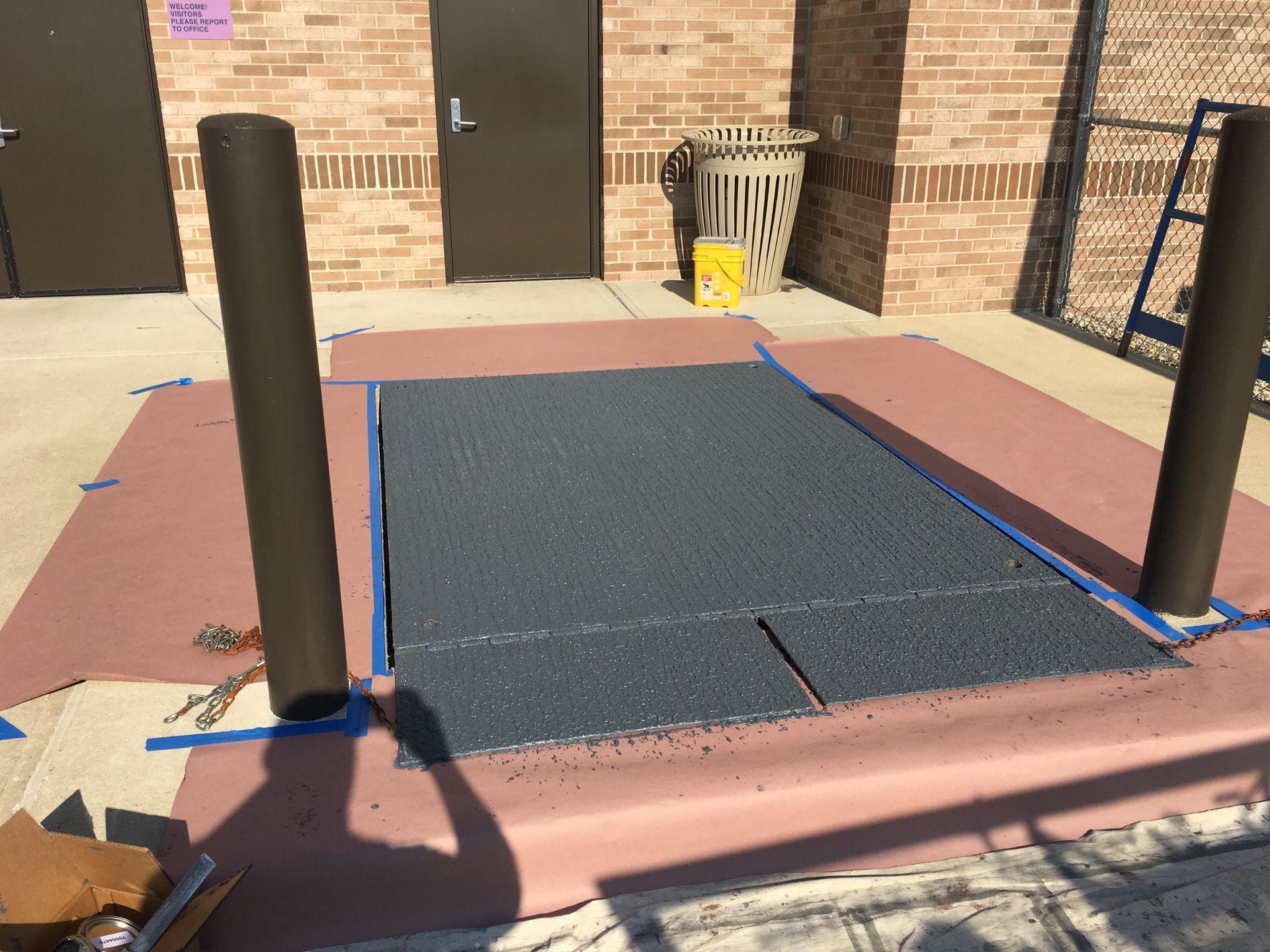 Outdoor wheelchair lift platform with black posts beside a brick building entrance.