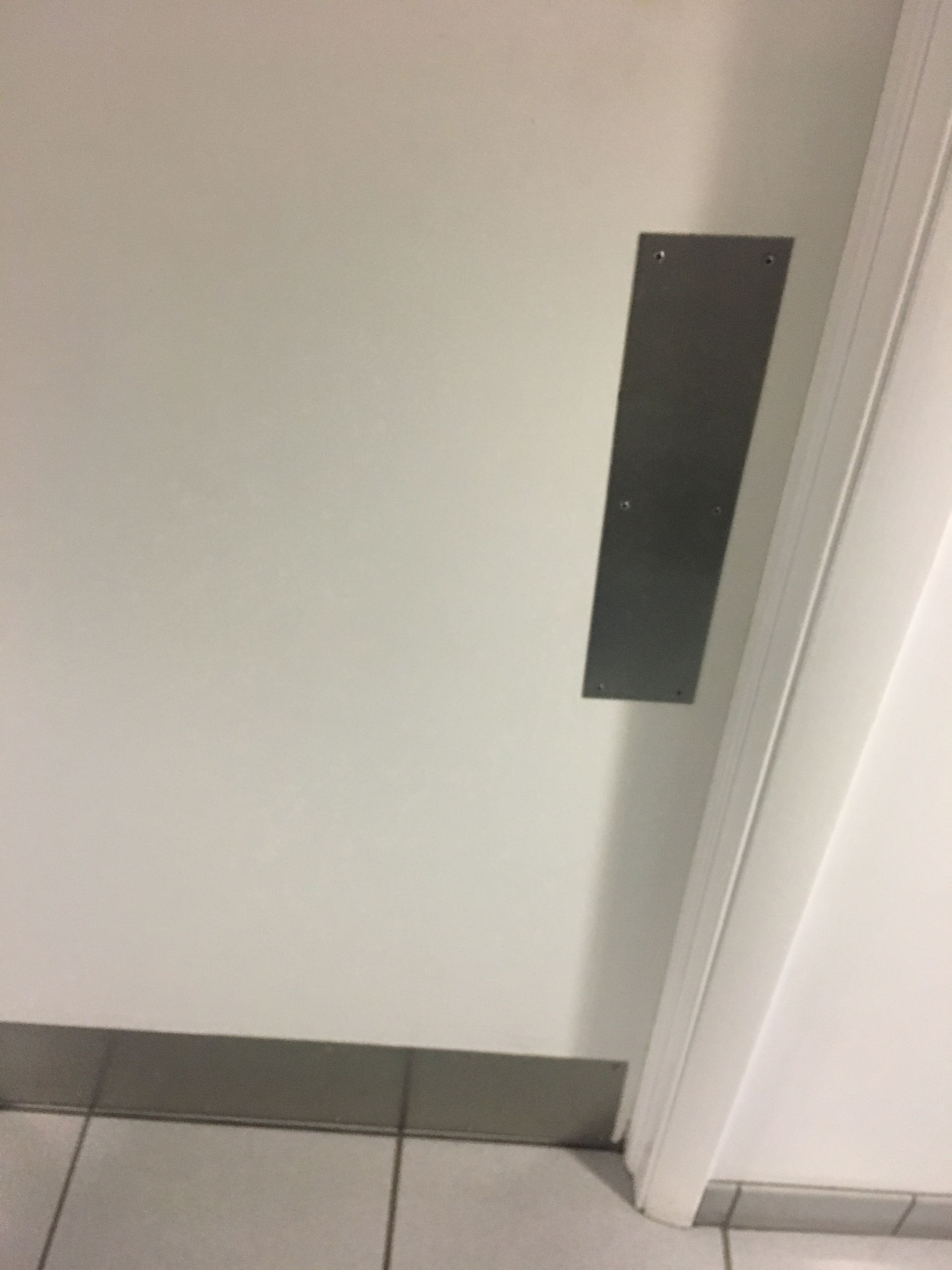 White wall with a black rectangular fixture beside a doorway and tiled floor.