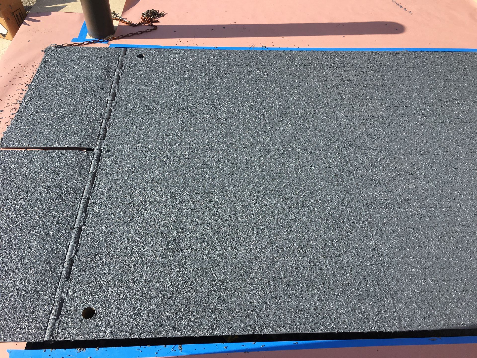 Black textured mat or ramp edge on a pink floor, with a person’s legs partly visible at the top left.