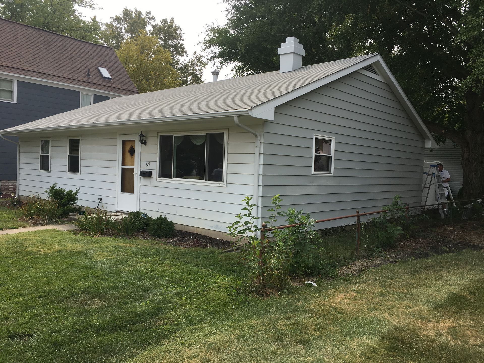 White single-story house with gray siding and metal roof, viewed from a grassy yard.
