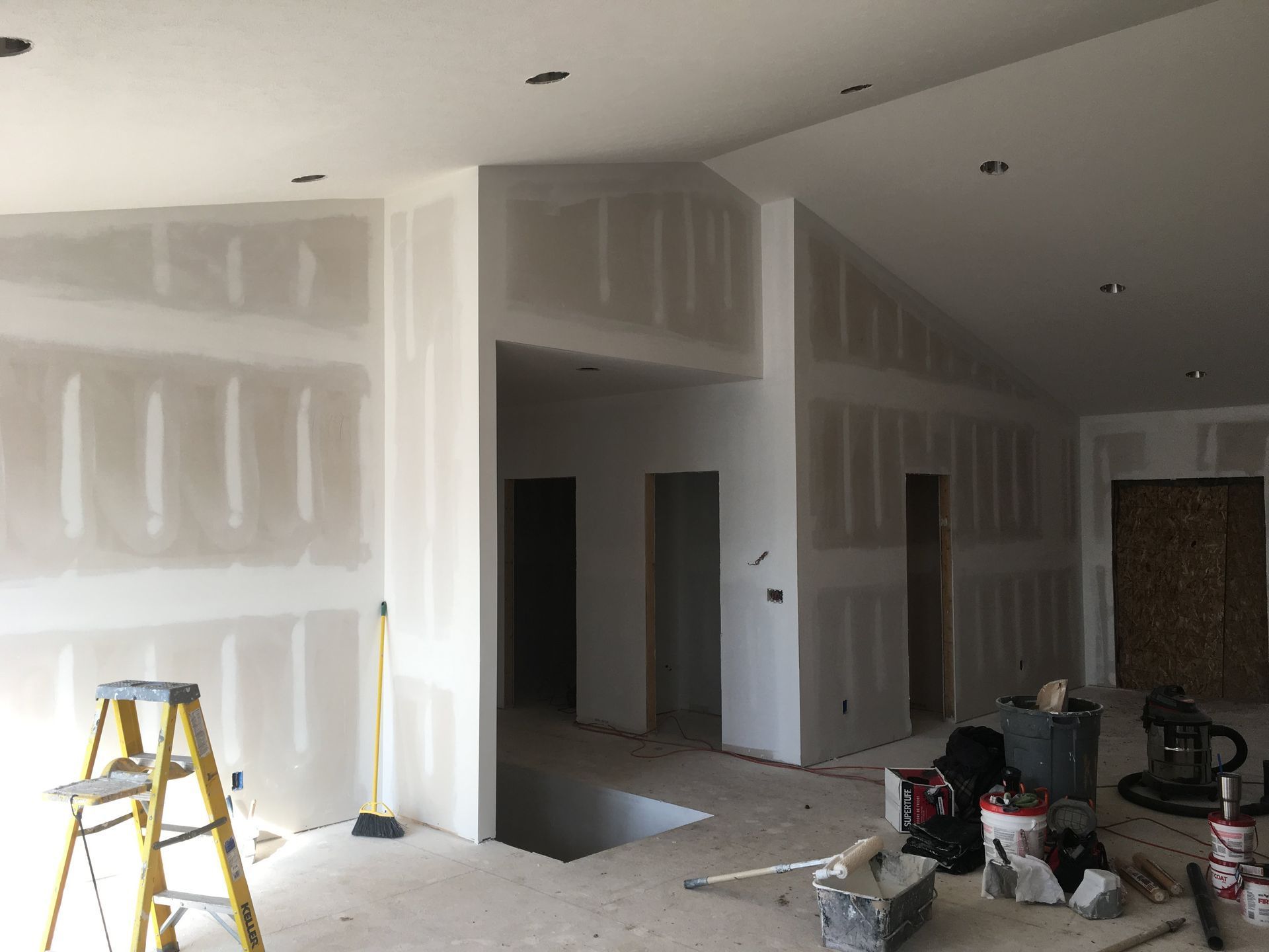 Unfinished interior with drywall, ladders, and tools in a room under construction.