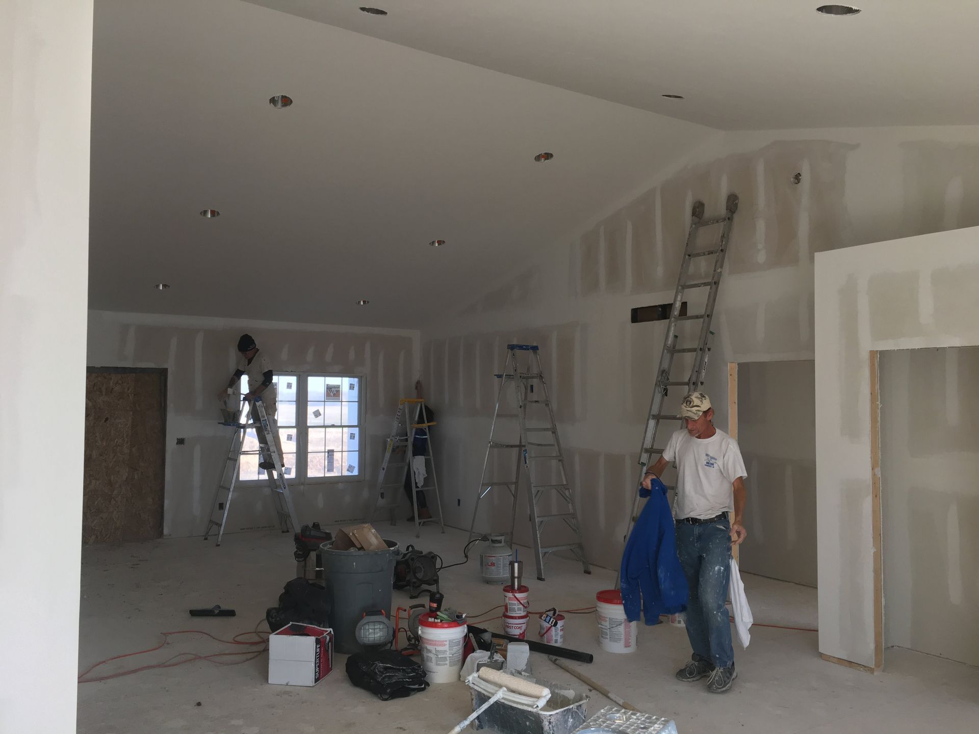 Workers painting a room under construction with ladders, tools, and open drywall visible