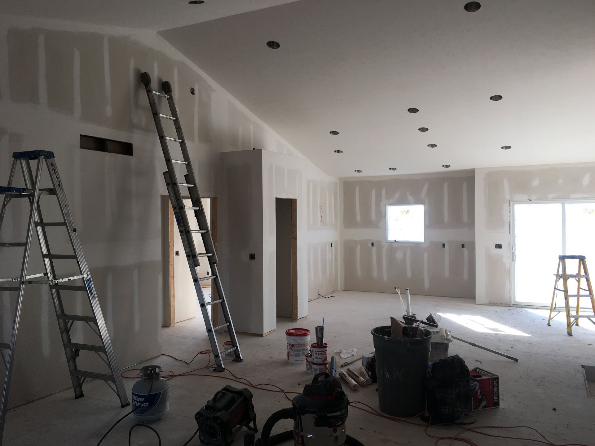 Renovation room with drywall, ladders, tools, and bright sunlight from windows