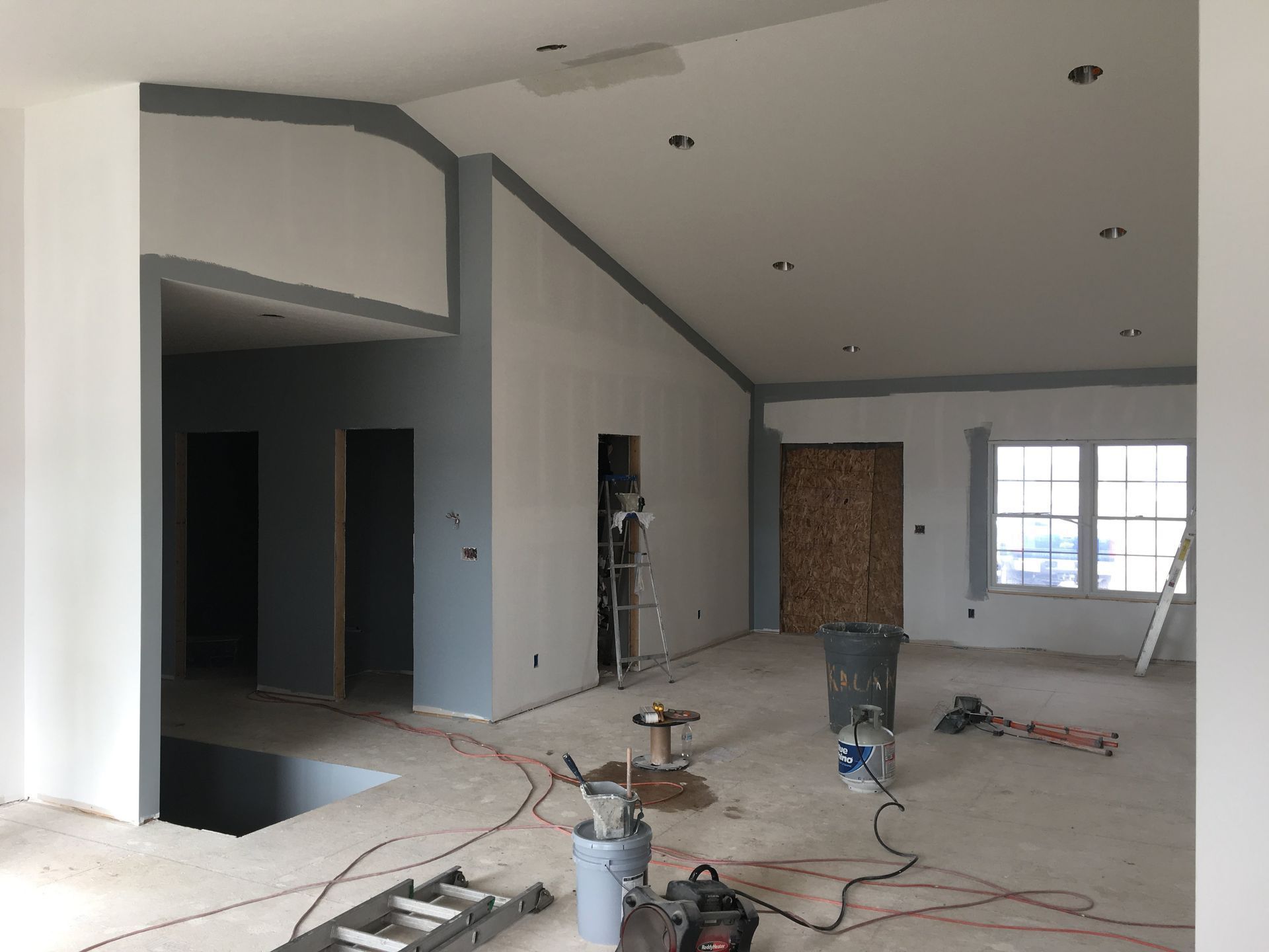 Unfinished interior room with exposed wiring, ceiling lights, and construction tools on the floor