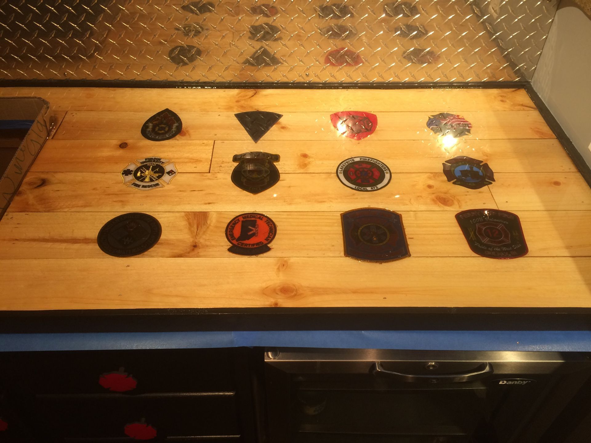 Wooden countertop with assorted small patches and pins arranged in rows under warm light