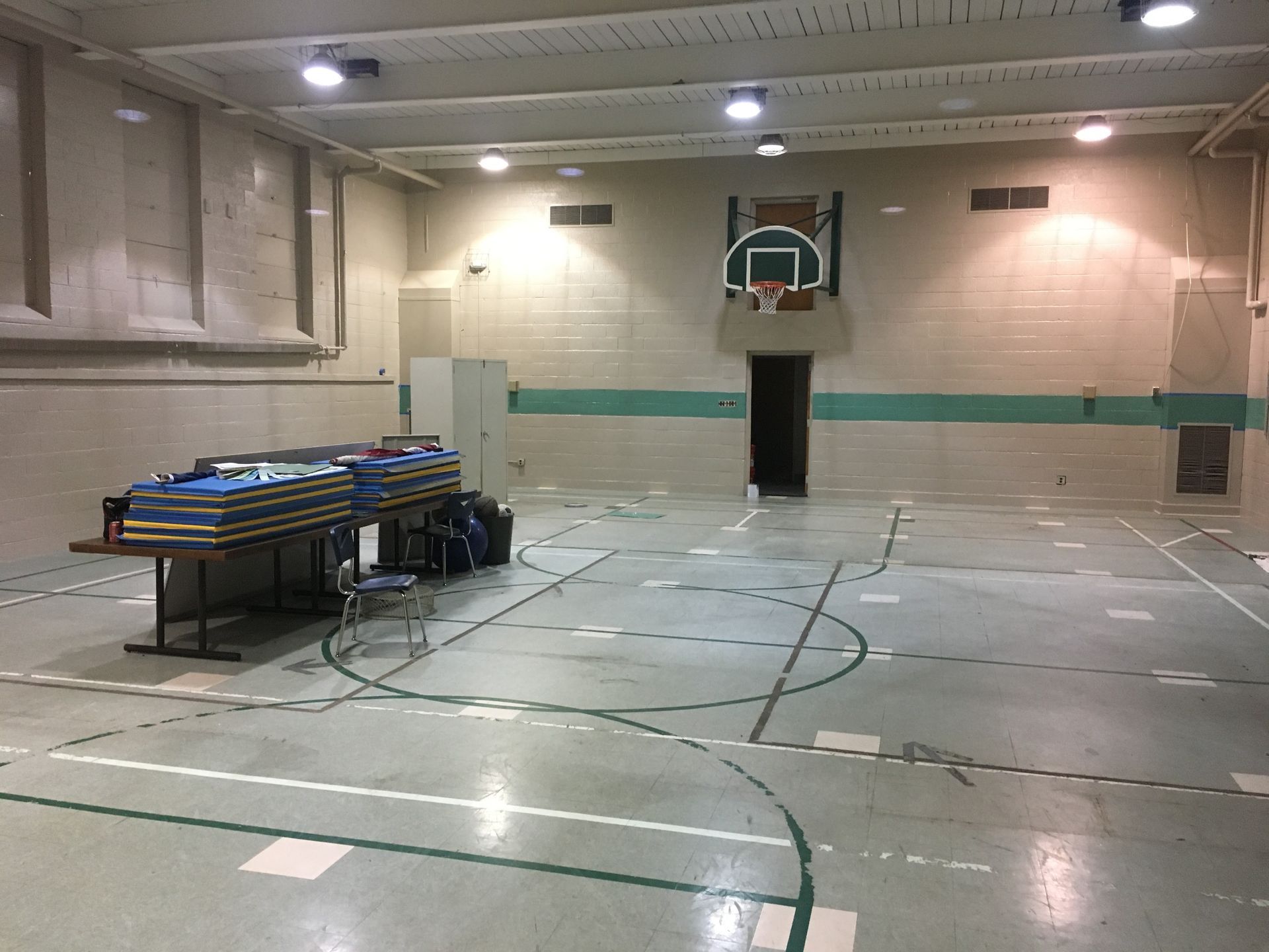 Empty gymnasium with a basketball hoop and stacked folding tables on the left.