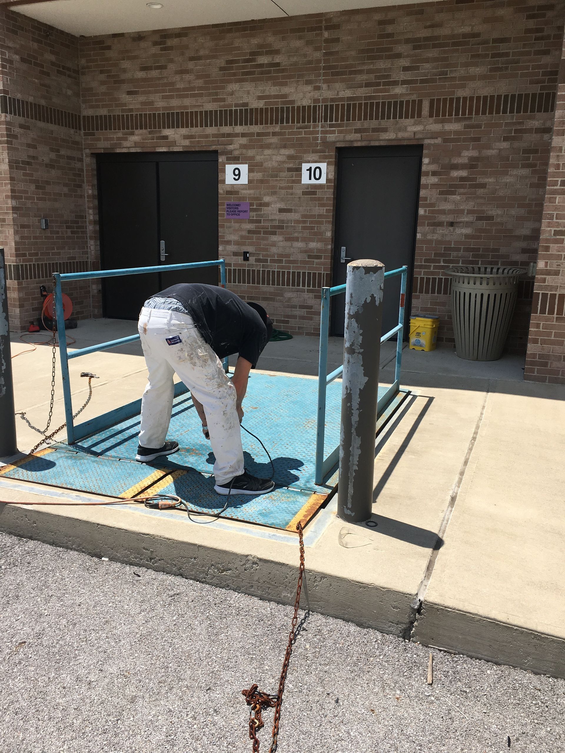Person bending over a platform lift outside a brick building with accessible parking signs.