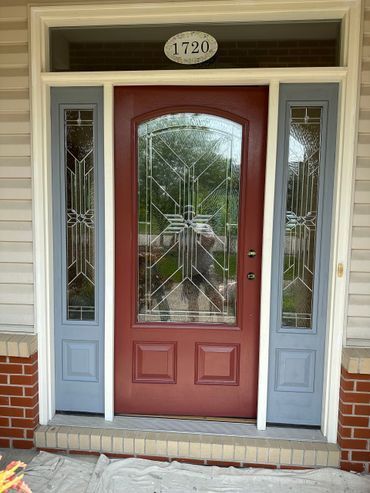 Red front door with glass sidelights and transom, framed by blue trim and brick steps.