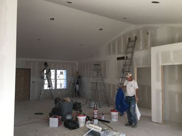 Workers standing in a large unfinished room with ladders, tools, and construction materials.
