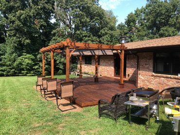 Backyard deck with pergola, patio furniture, and a brick house beside a green lawn and trees