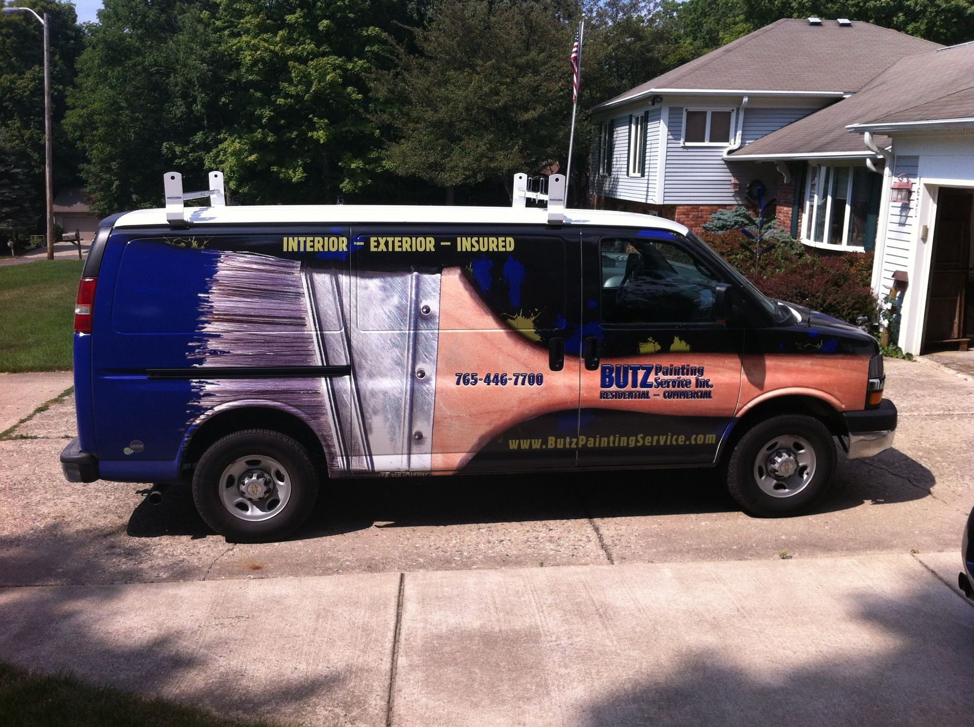 Painted work van parked in a driveway, with ladder racks and business ads on the sides.