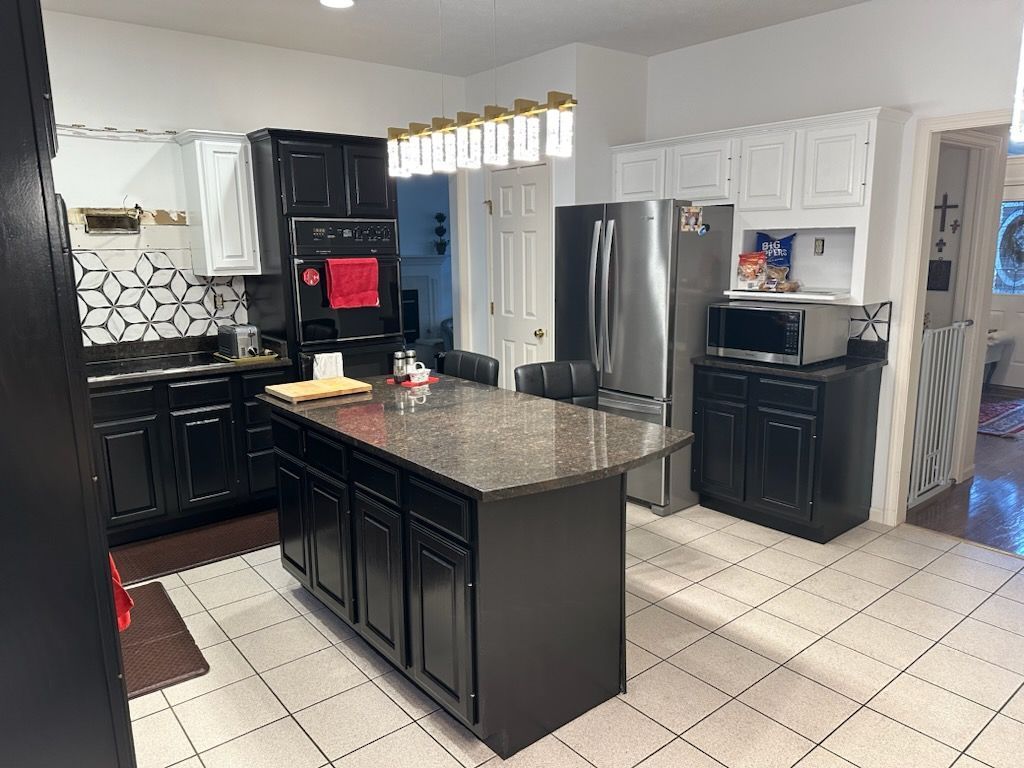 Modern kitchen with black cabinets, stainless steel refrigerator, granite island, and white tile floor