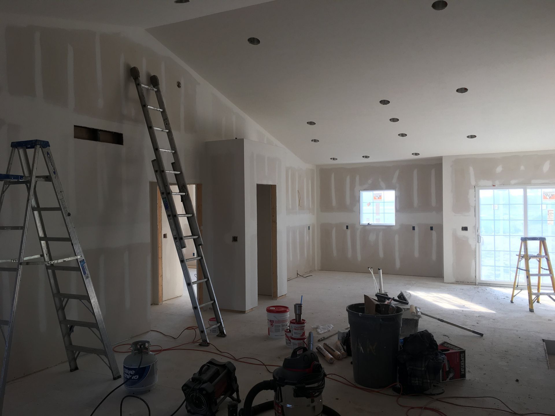 Unfinished room with drywall, ladders, tools, and bright windows during renovation