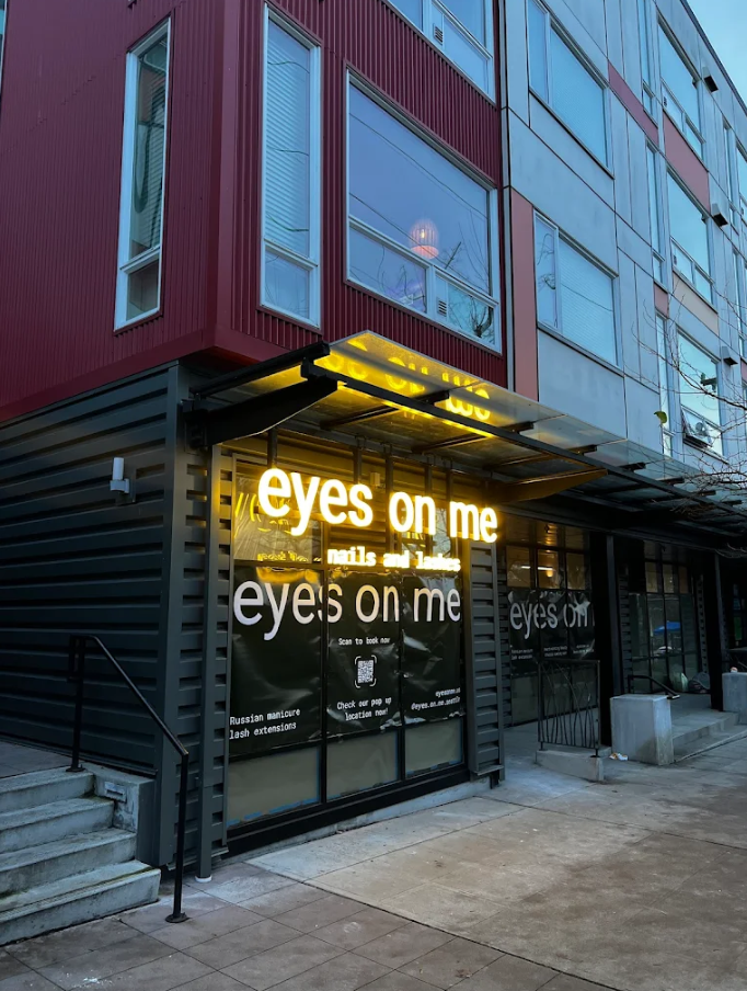 Storefront with illuminated “eyes on me” sign on a modern building exterior.