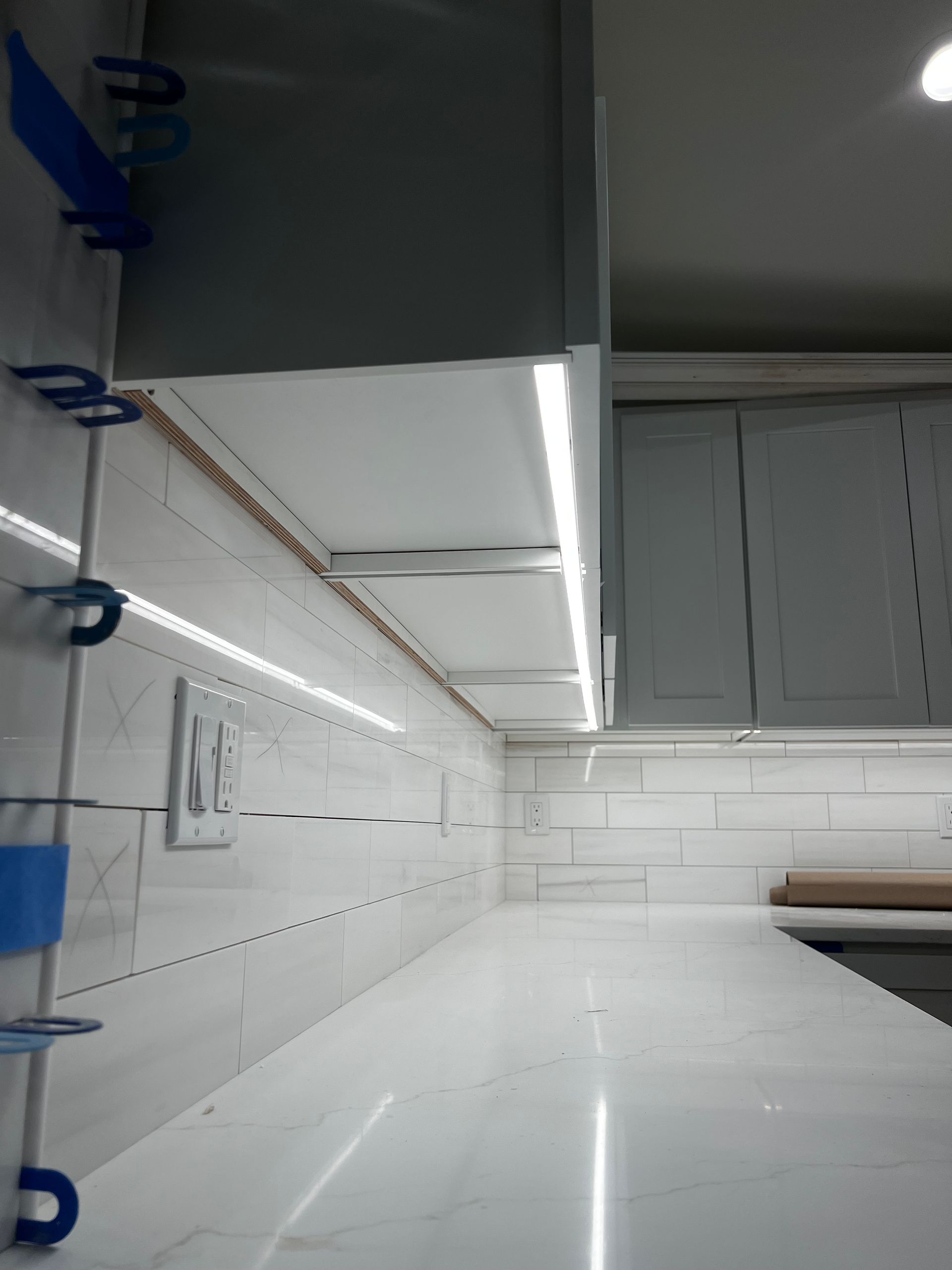 White kitchen with glossy countertops, white cabinets, and blue shelf brackets along the left wall.