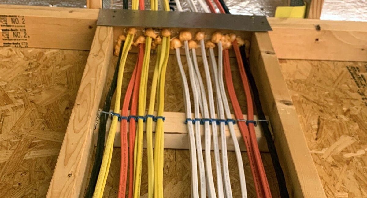 Bundle of multicolored electrical cables routed through a wall opening under a wooden beam