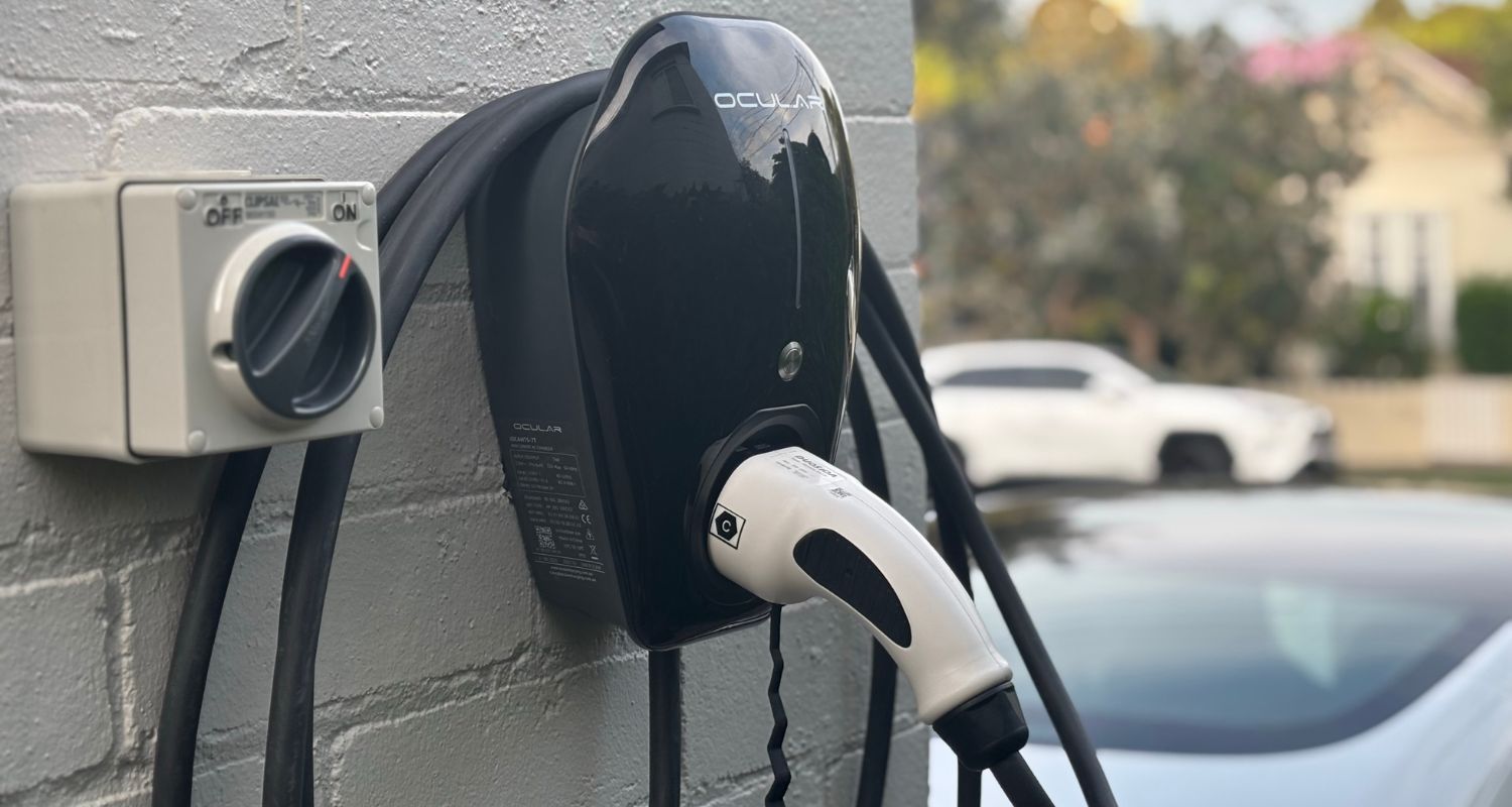 Electric vehicle charging station mounted on a gray wall with a white charging plug connected.