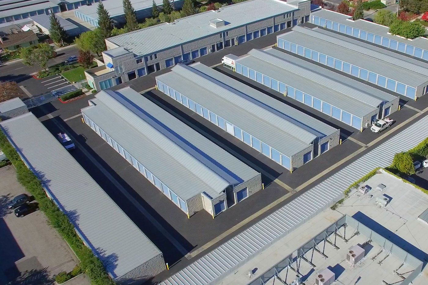 Aerial view of a storage facility with multiple rows of gray metal buildings and blue doors.