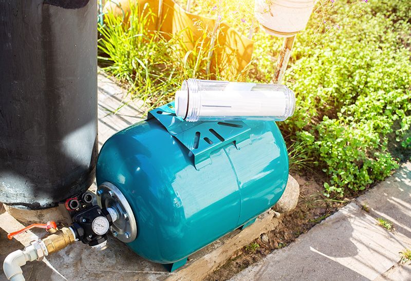 A water pump is sitting on a sidewalk next to a black tank.