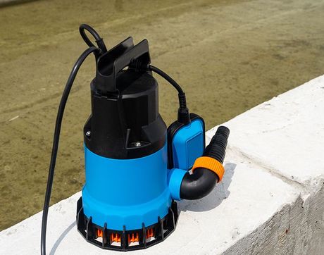 A blue and black water pump is sitting on a concrete wall.
