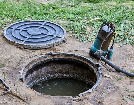A manhole cover with a pump attached to it is open and filled with water.