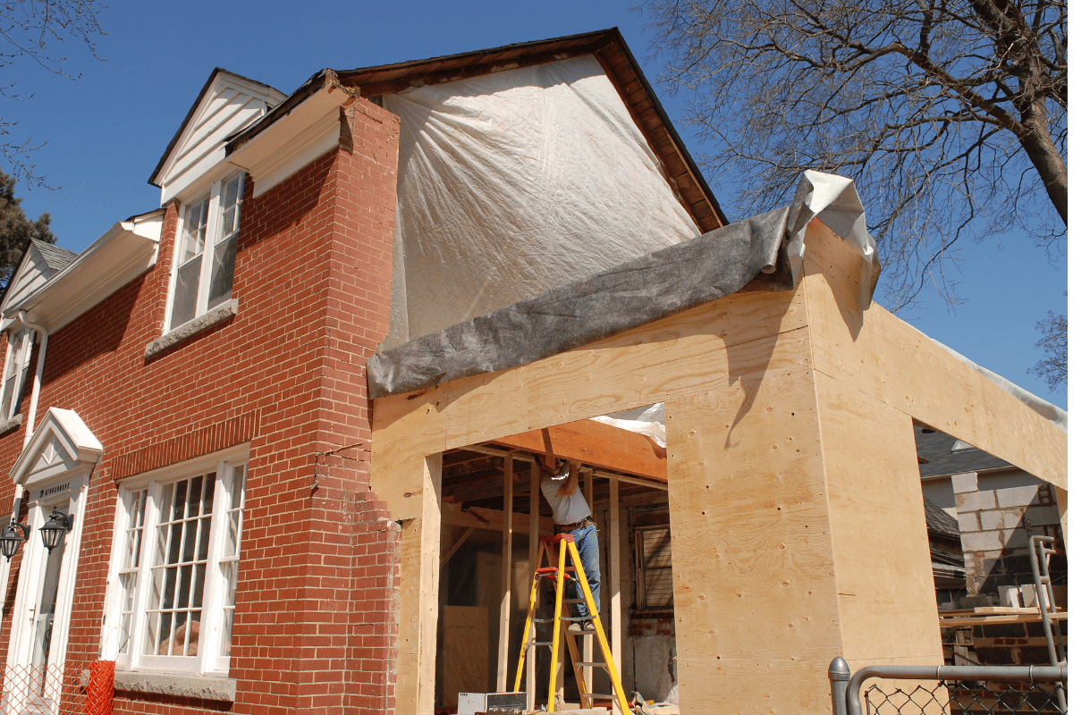 Brick house with a beige-framed front porch under construction, with ladders and exposed insulation.