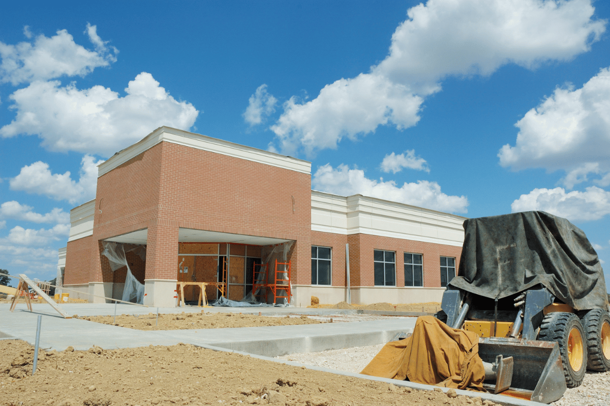 Partially built brick building under construction with equipment and materials in front, beneath a blue sky