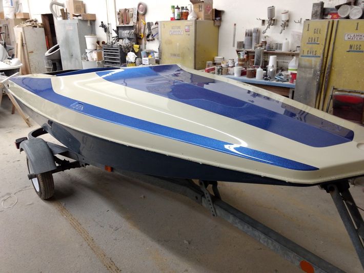 Blue and white speedboat on a trailer in a workshop, surrounded by tools and equipment