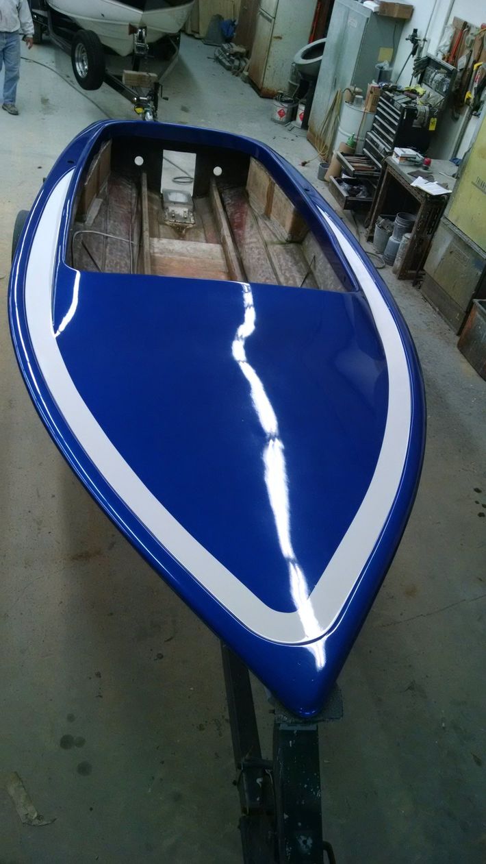 Blue boat hull in a workshop, viewed from above on a stand.