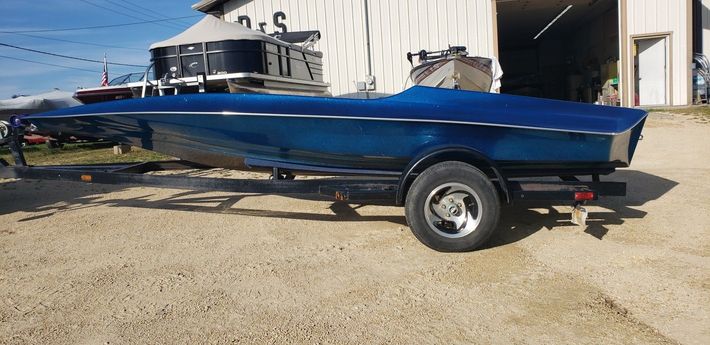 Blue motorboat on a trailer parked on gravel in front of a building.