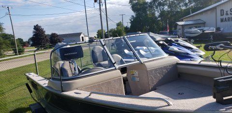 Beige motorboat on a trailer parked outdoors beside a road and buildings.
