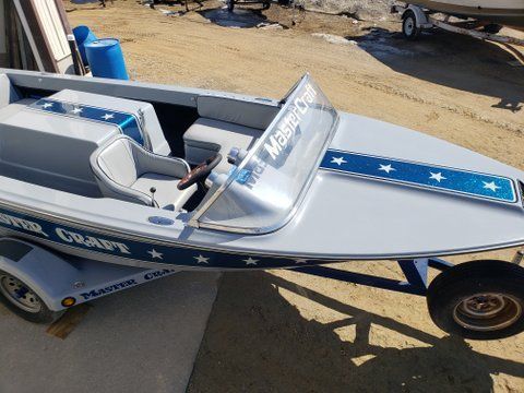 Silver racing boat on a trailer with blue star-striped deck, parked on a ramp.