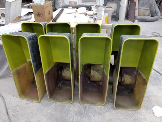 Green metal duct sections stacked on a workshop floor with cardboard boxes in the background