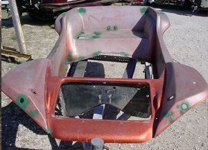 Damaged red and pink car body shell resting outdoors on gravel