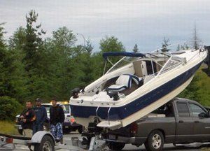 Boat on a trailer being towed by a pickup truck, with several people standing nearby outdoors.