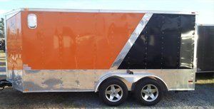 Orange and black enclosed cargo trailer with silver trim and dual axles, parked outdoors.