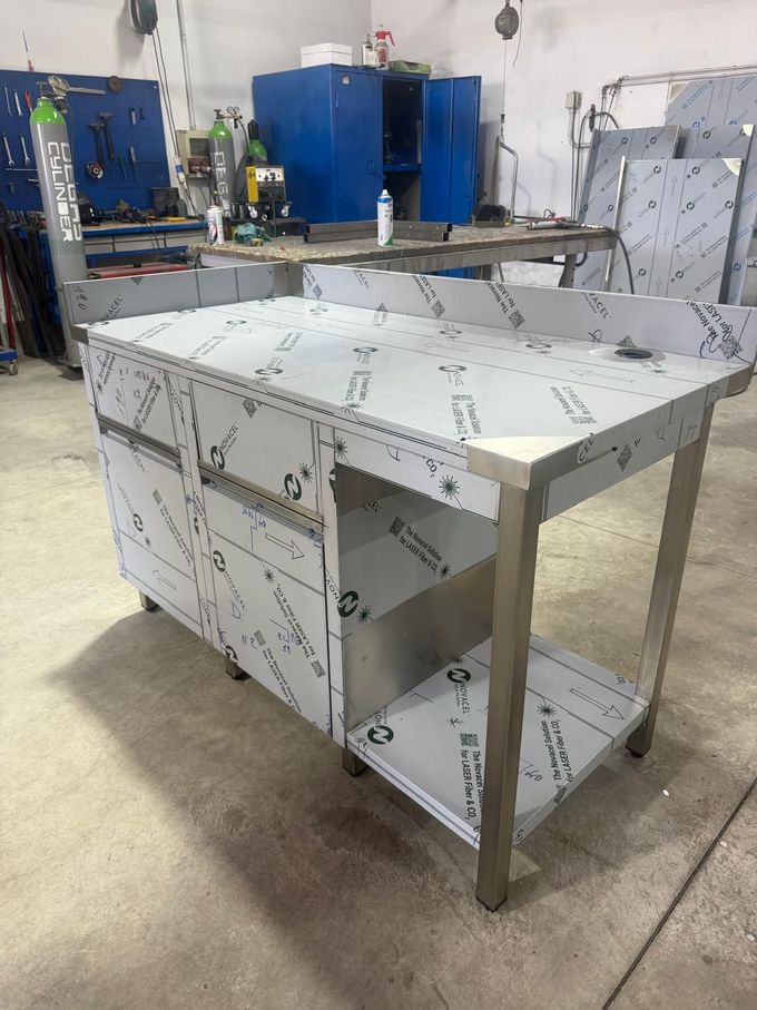 Struttura di un banco da lavoro in metallo con pannelli bianchi non rifiniti in un'officina, con attrezzature blu sullo sfondo.