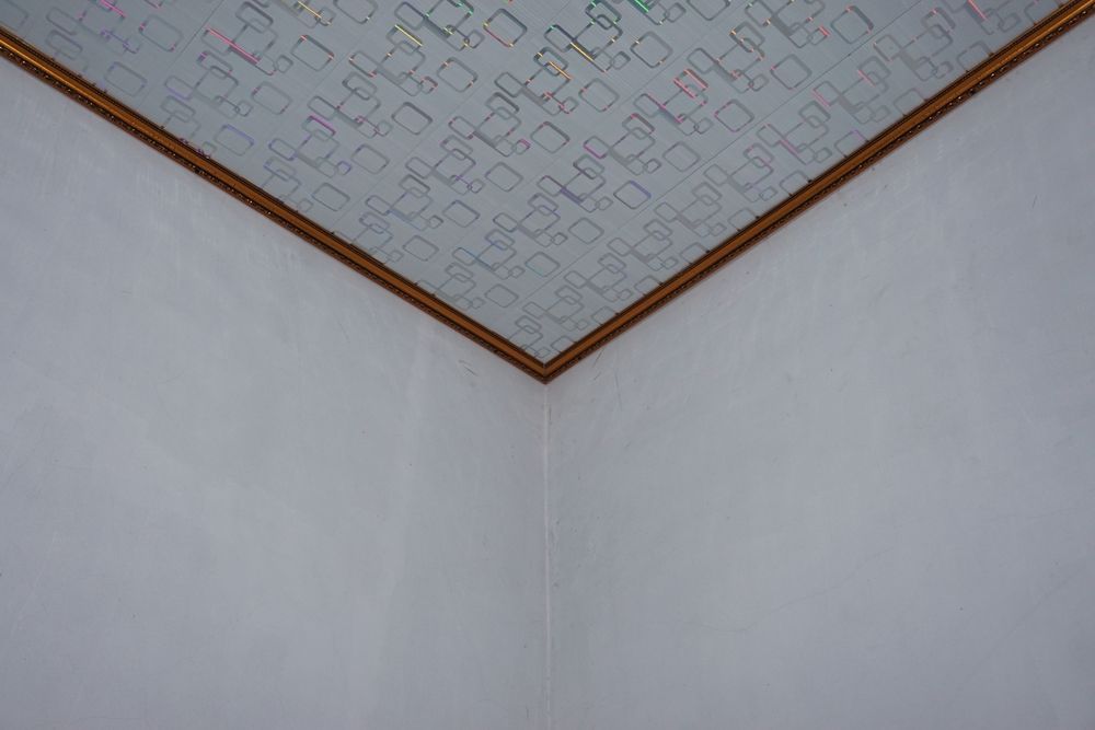 Corner of a white-walled room with a patterned ceiling framed by a brown border.