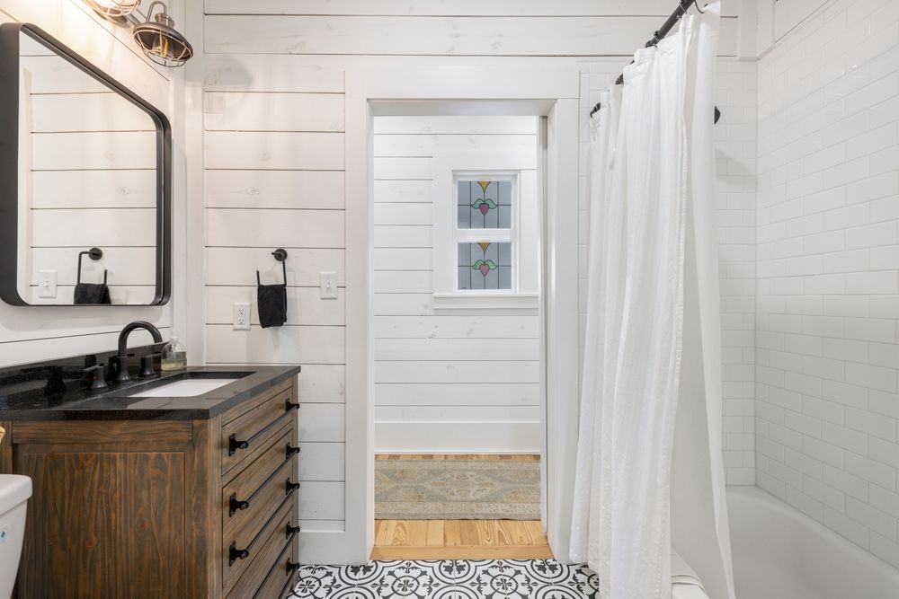 Bathroom with white shiplap walls, wood vanity with black fixtures, and patterned floor.