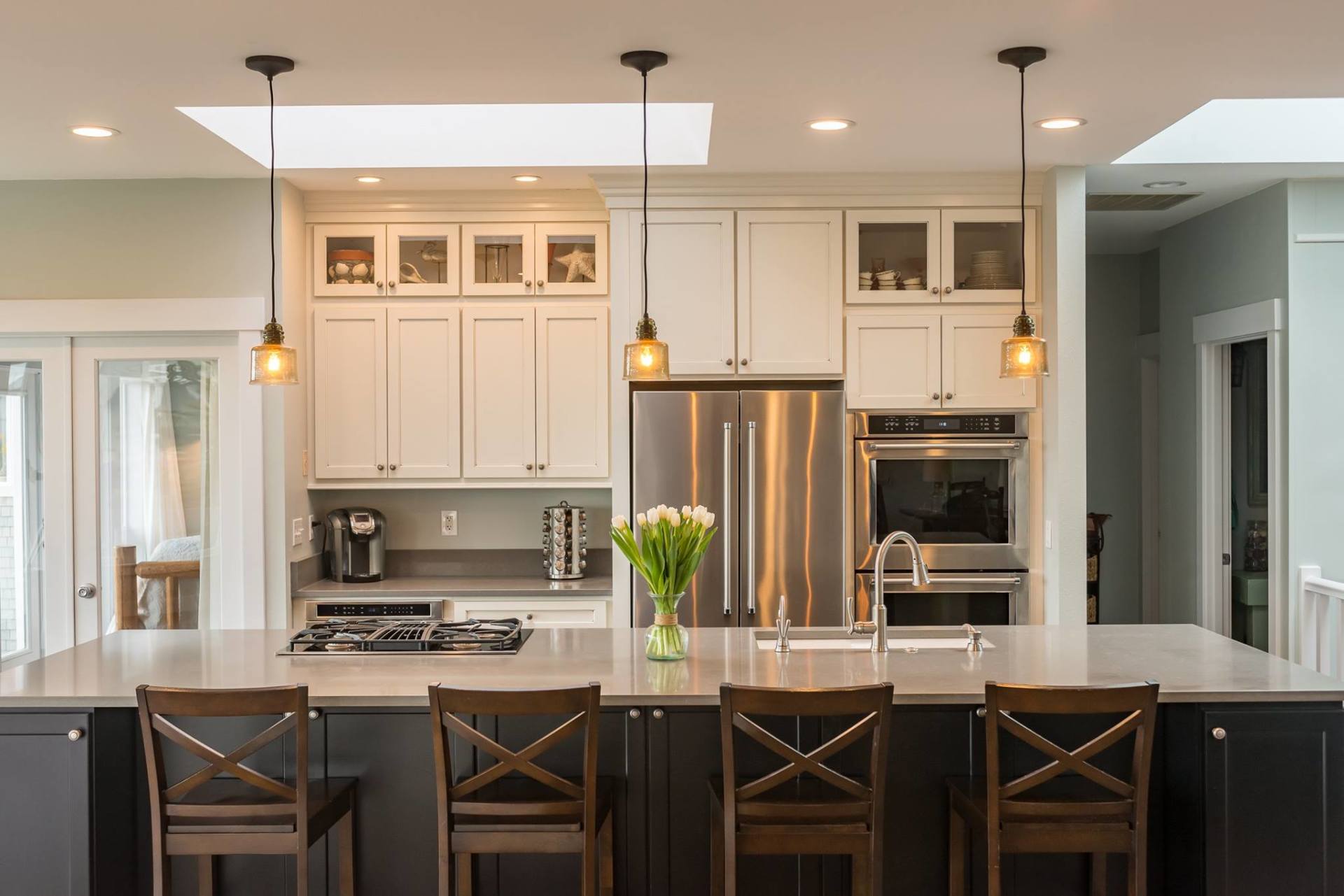 Modern white kitchen with island, pendant lights, stainless steel appliances, and bar stools