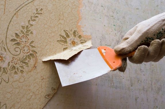 Hand using a putty knife to scrape old wallpaper from a wall